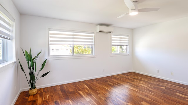 empty room with a wall mounted AC, wood finished floors, ceiling fan, and baseboards