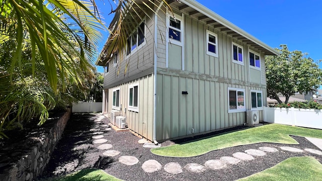 view of home's exterior featuring board and batten siding, ac unit, a yard, and fence