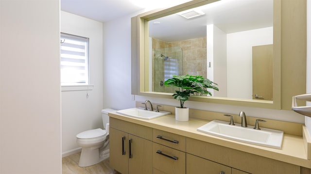 full bath with a sink, a tile shower, double vanity, and toilet