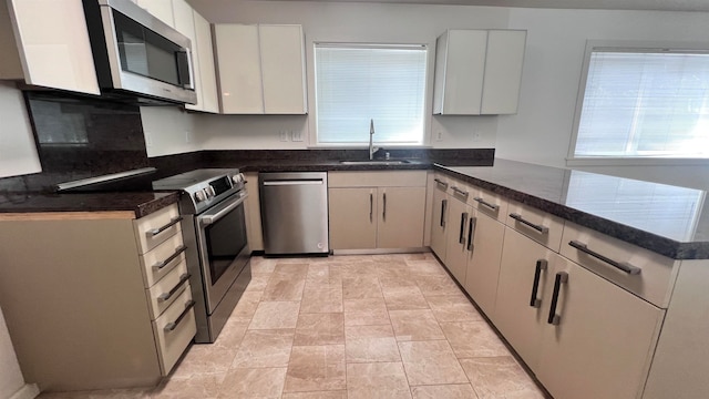 kitchen featuring stainless steel appliances, white cabinets, kitchen peninsula, sink, and dark stone countertops