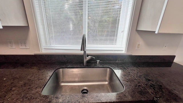 details featuring dark stone counters, sink, and white cabinets