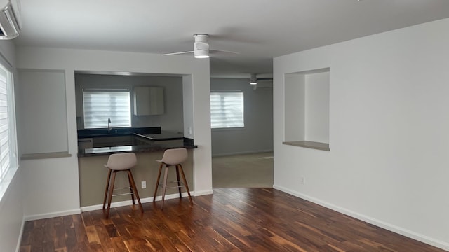 kitchen featuring ceiling fan, dark countertops, wood finished floors, and a kitchen breakfast bar