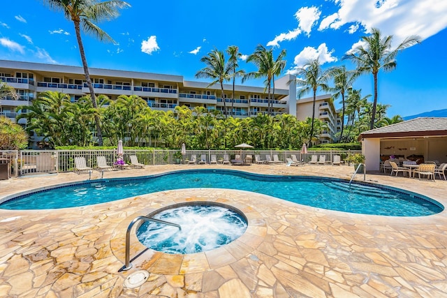 pool with a patio, a community hot tub, and fence