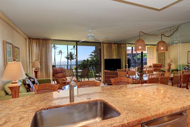 kitchen with a sink, ceiling fan, open floor plan, light stone countertops, and dishwasher