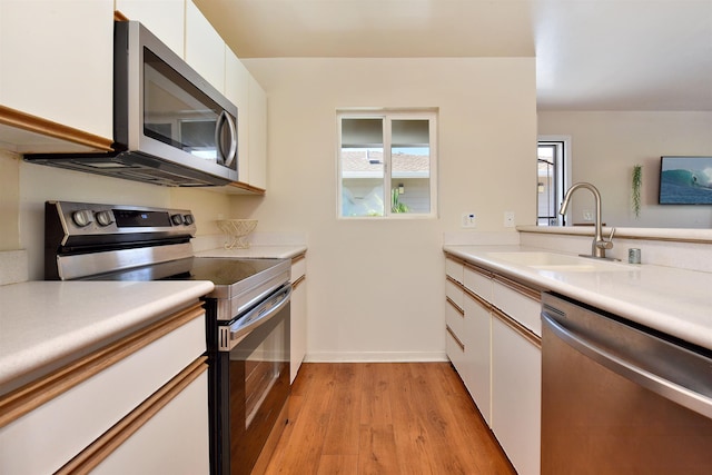 kitchen with light wood finished floors, a sink, stainless steel appliances, light countertops, and white cabinets