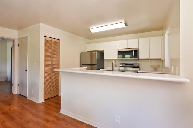 kitchen featuring wood finished floors, white cabinetry, stainless steel appliances, a peninsula, and light countertops