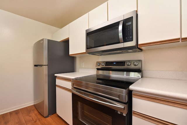 kitchen featuring light wood finished floors, baseboards, light countertops, stainless steel appliances, and white cabinetry