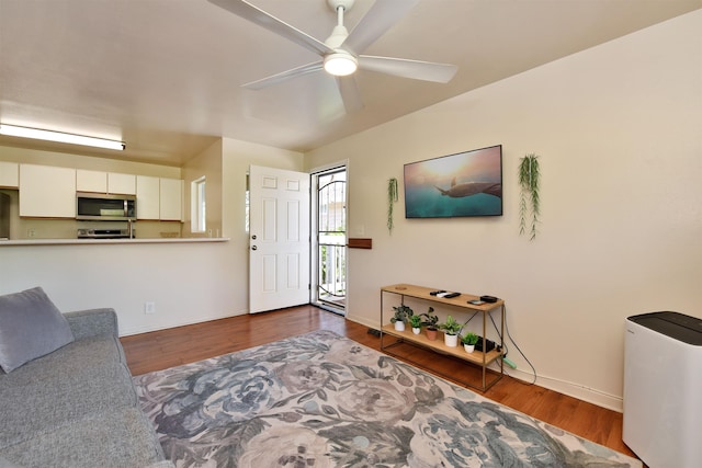 living area with a ceiling fan, wood finished floors, and baseboards