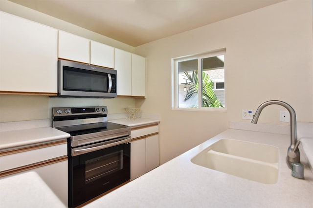 kitchen with a sink, appliances with stainless steel finishes, white cabinets, and light countertops