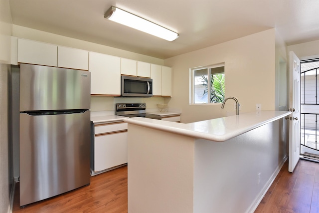 kitchen featuring a peninsula, white cabinets, light wood finished floors, and stainless steel appliances