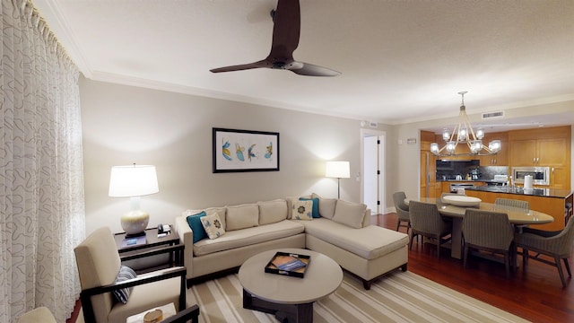 living room featuring light wood finished floors, crown molding, visible vents, baseboards, and ceiling fan with notable chandelier