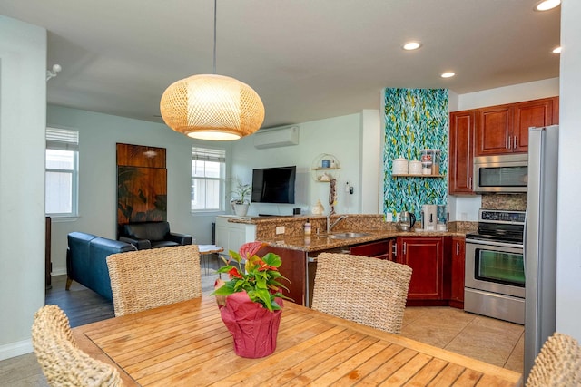 kitchen with open floor plan, a peninsula, stainless steel appliances, a wall mounted AC, and a sink