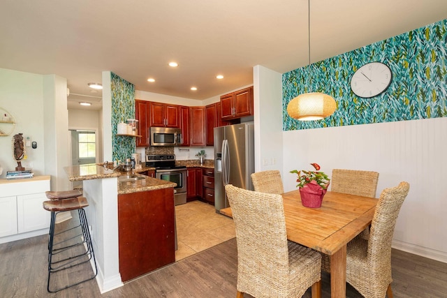 kitchen with wallpapered walls, a peninsula, a sink, stainless steel appliances, and reddish brown cabinets