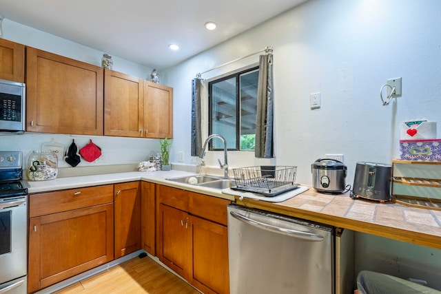 kitchen with light hardwood / wood-style floors, appliances with stainless steel finishes, tile countertops, and sink