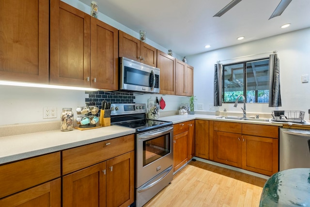 kitchen with light wood-type flooring, sink, decorative backsplash, appliances with stainless steel finishes, and ceiling fan