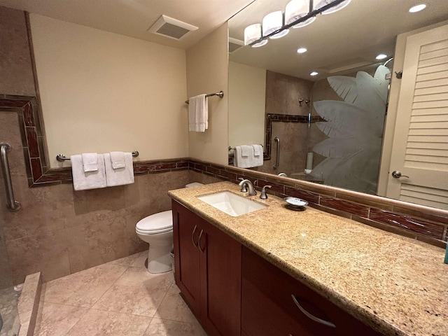 bathroom with vanity, visible vents, tiled shower, tile walls, and toilet