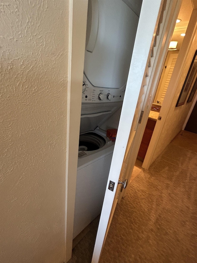 clothes washing area featuring carpet flooring, stacked washer / dryer, laundry area, and a textured wall