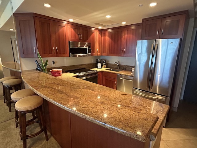 kitchen with light stone countertops, a peninsula, recessed lighting, a sink, and appliances with stainless steel finishes