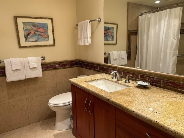 bathroom with tile walls, toilet, wainscoting, tile patterned floors, and vanity