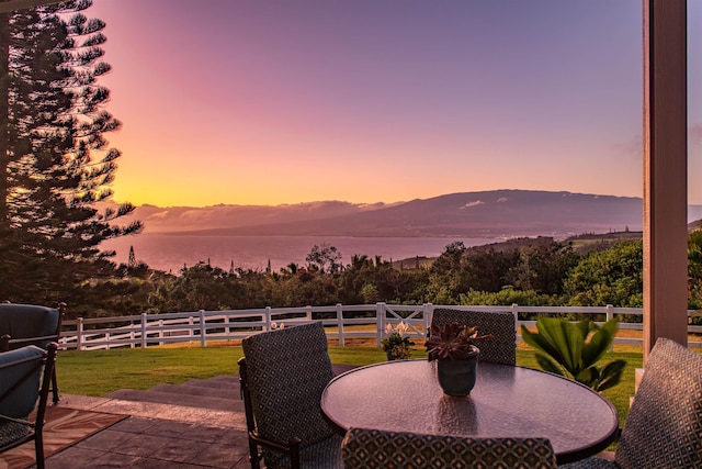 patio terrace at dusk featuring a water and mountain view and a yard