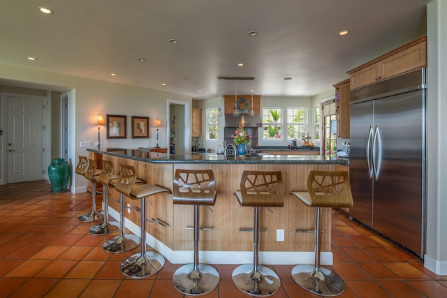 kitchen featuring a spacious island, a kitchen bar, dark tile patterned floors, built in refrigerator, and dark stone counters