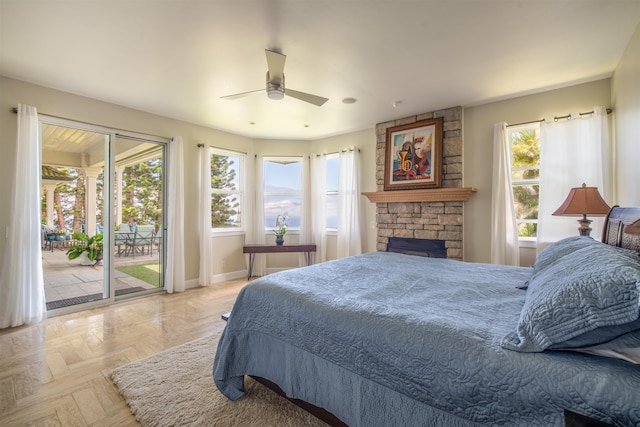 bedroom featuring light parquet floors, a stone fireplace, ceiling fan, access to outside, and multiple windows