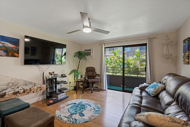 living room featuring a wall mounted AC, a textured ceiling, light hardwood / wood-style floors, and ceiling fan