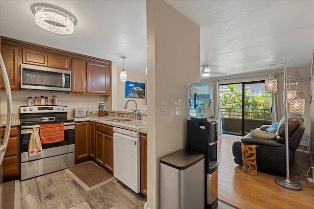 kitchen featuring sink, stainless steel appliances, pendant lighting, wood-type flooring, and ceiling fan with notable chandelier