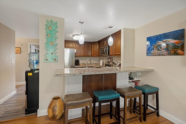 kitchen featuring pendant lighting, a kitchen breakfast bar, dark hardwood / wood-style floors, kitchen peninsula, and stainless steel appliances