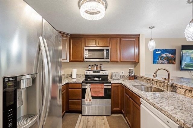 kitchen featuring sink, hanging light fixtures, light stone counters, kitchen peninsula, and stainless steel appliances