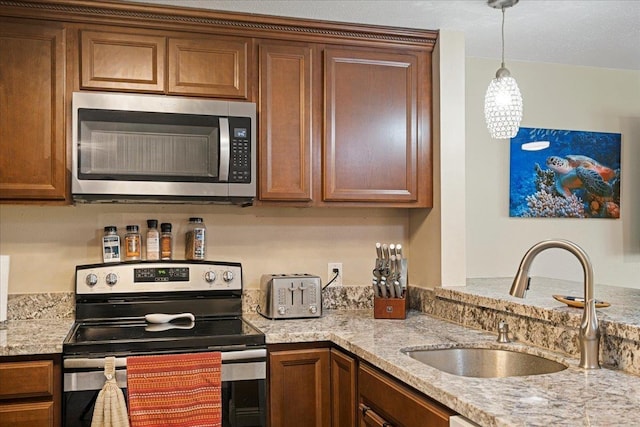 kitchen featuring light stone countertops, sink, stainless steel appliances, and decorative light fixtures