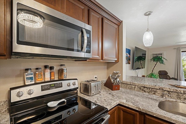 kitchen with light stone countertops, pendant lighting, stainless steel appliances, and sink