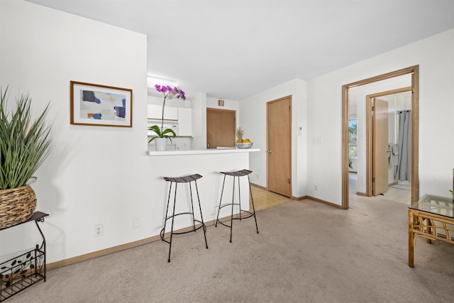 interior space featuring light carpet, white cabinets, kitchen peninsula, and a breakfast bar