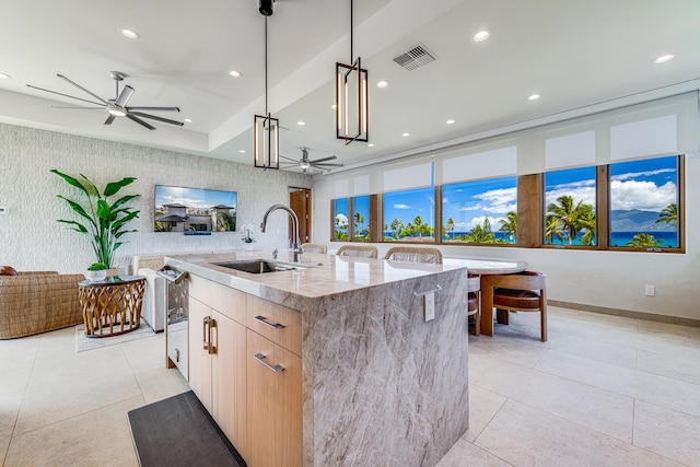 kitchen featuring ceiling fan, sink, a center island with sink, and light stone countertops