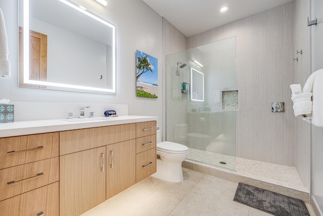 bathroom with tile patterned flooring, vanity, tiled shower, and toilet