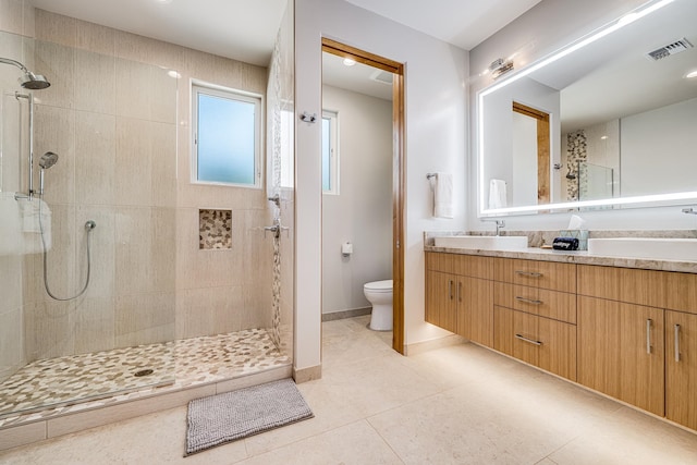 bathroom featuring toilet, vanity, tiled shower, and tile patterned floors