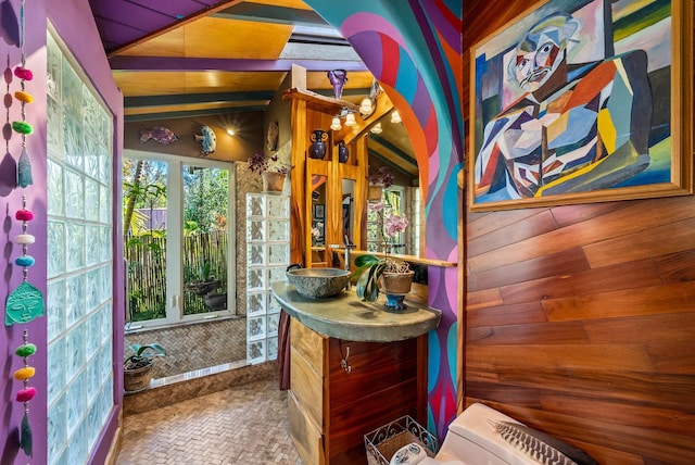 bathroom with vanity, toilet, lofted ceiling, and wood walls