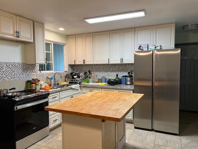 kitchen featuring backsplash, a center island, light tile patterned flooring, stainless steel appliances, and wood counters