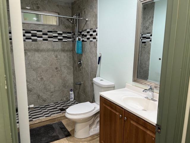 bathroom featuring toilet, vanity, a tile shower, and tile patterned flooring