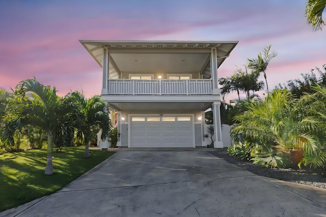 raised beach house featuring a garage, a front yard, driveway, and a balcony