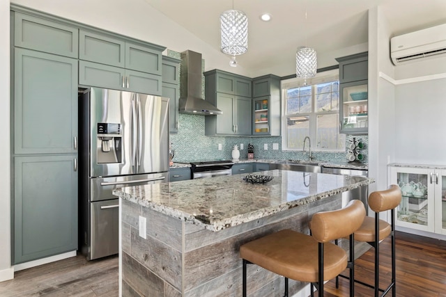 kitchen featuring appliances with stainless steel finishes, light stone counters, a wall mounted air conditioner, decorative light fixtures, and wall chimney range hood