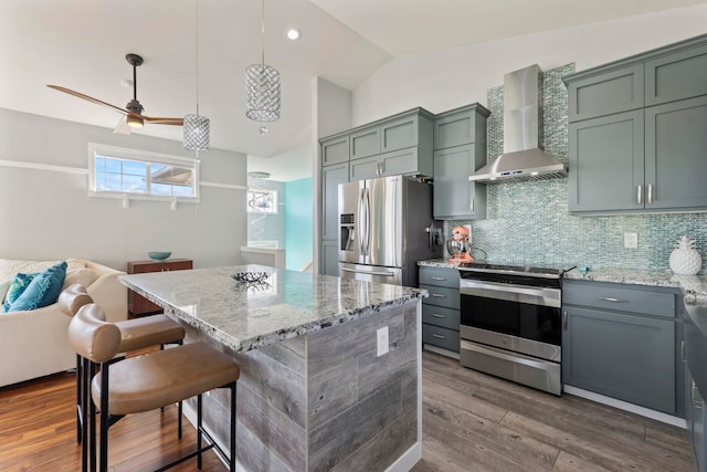 kitchen with wall chimney range hood, appliances with stainless steel finishes, light stone counters, and a center island