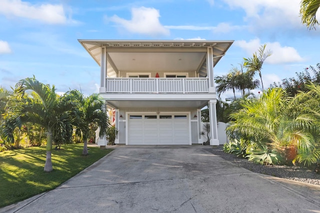 coastal home featuring an attached garage, concrete driveway, a front yard, and a balcony