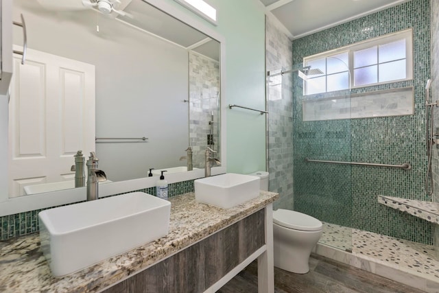 bathroom featuring wood finished floors, tiled shower, a sink, and toilet