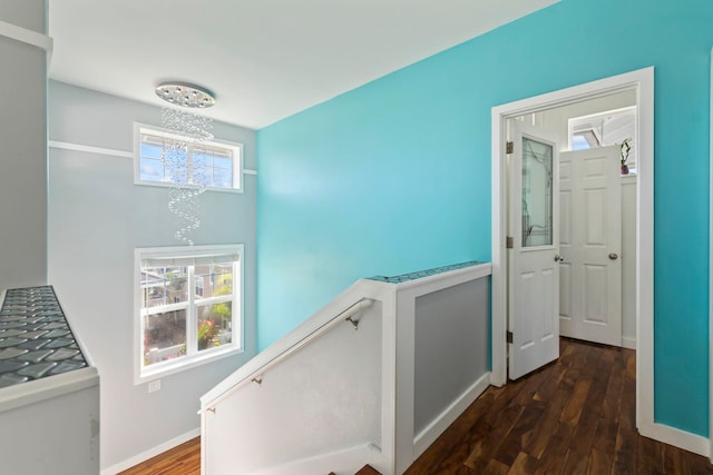 corridor featuring a notable chandelier, baseboards, dark wood-type flooring, and an upstairs landing