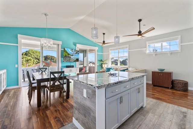 kitchen with dark wood finished floors, lofted ceiling, a center island, hanging light fixtures, and light stone countertops