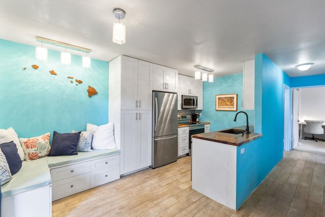 kitchen featuring light wood-style flooring, stainless steel appliances, a sink, white cabinets, and wooden counters