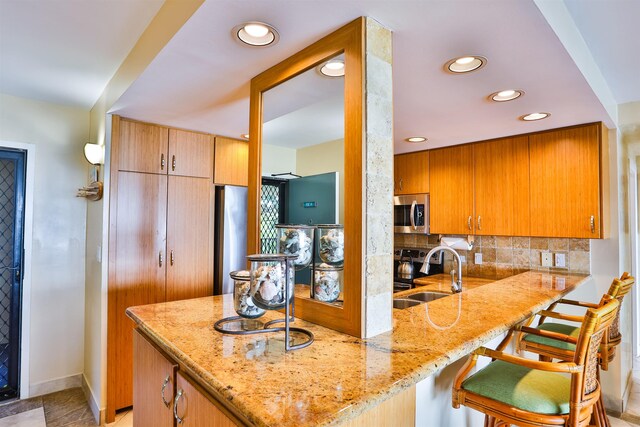 kitchen with kitchen peninsula, tasteful backsplash, a breakfast bar, sink, and stainless steel appliances