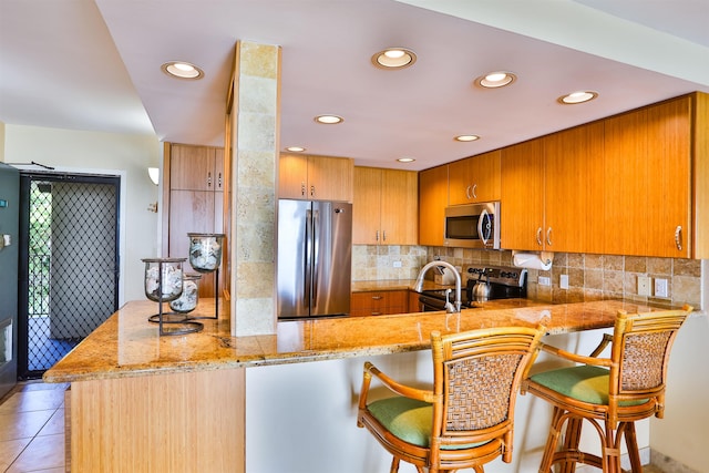 kitchen featuring kitchen peninsula, a breakfast bar, light stone countertops, light tile patterned floors, and appliances with stainless steel finishes