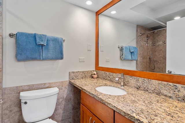 bathroom with tile walls, tiled shower, toilet, and oversized vanity